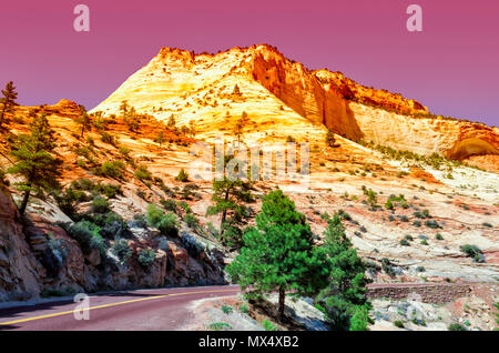 Rosa Sonnenuntergang über Gelb, Orange und Weiß Sandstein Berge; gebogene Straße mit steinernen Brücke und grüne Bäume auf der rechten Seite der Straße. Stockfoto