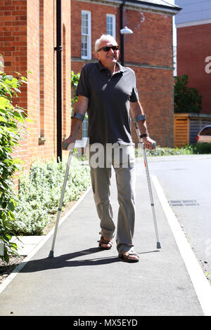 Ein älterer Mann im Bild gehen mit Krücken auf einem schlechten Bein in Chichester, West Sussex, UK. Stockfoto