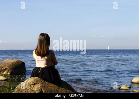 Mädchen sitzt auf einem Stein, am blauen Meer. Sommer, Sonne, s Stockfoto