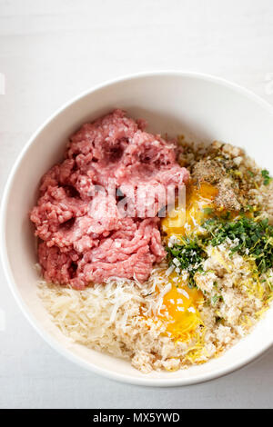 Frikadellen Zutaten in die Schüssel geben. Gehacktes Schweinefleisch, Gewürze, Kräuter, Paniermehl, Eigelb und Parmesan. Stockfoto