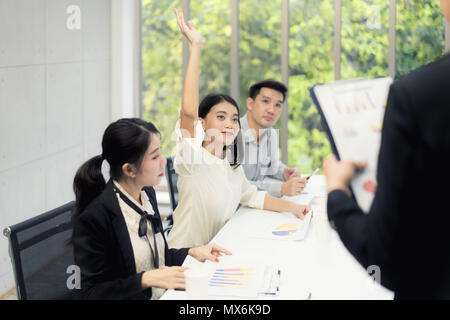 Asiatische Frau heben ihre Hände hat Frage während Geschäftsmann Präsentation über Business Verkauf Bericht auf der Tagung Zimmer Stockfoto