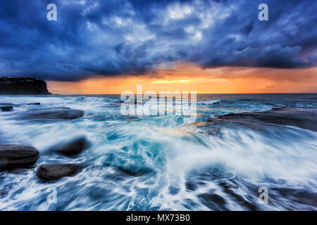 Stürmisches Wetter von offenen Pazifischen Ozean bei bungan Strand von Sydney Northern Beaches mit orange Rising Sun unter dicken Wolken. Stockfoto
