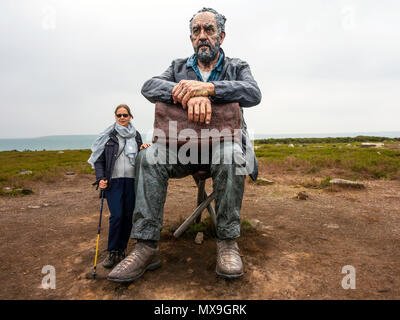 Eine ältere Frau, die von der sitzenden Mann Skulptur des Künstlers Sean Henry auf Castleton in der North Yorkshire Moors National Park mit Blick auf die westerdale Stockfoto