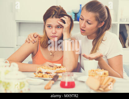 Junge Frau am Tisch mit Kuchen und beruhigende traurig Freund sitzen Stockfoto