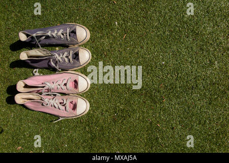 Ein paar rosa und blau Sneakers auf dem Rasen in der Sonne, vielleicht die männlichen und weiblichen Stockfoto