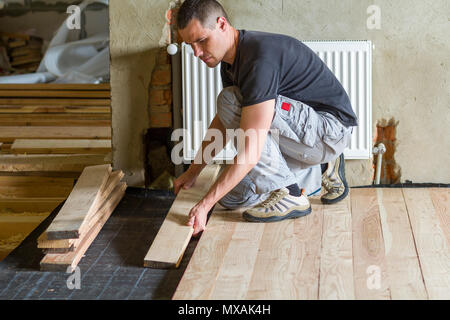 Junge schöne professionelle Tischler Installation von natürlichen hölzernen Planken auf Holzrahmen, in leeren unfertiges Zimmer unter Rekonstruktion. Improvemen Stockfoto