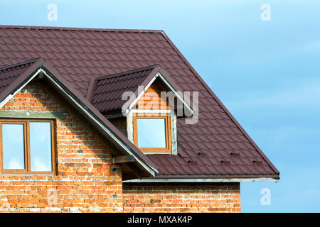 Close-up Detail Der neue brick House top mit braunen Schindeldach und Kunststoff Dachfenster auf der strahlend blaue Himmel Hintergrund. Immobilien und profe Stockfoto