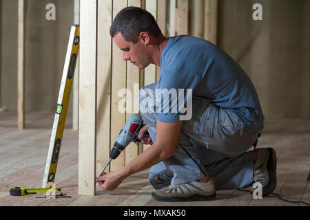 Junge professionelle Arbeiter verwendet und Schraubendreher Installation von Holzrahmen für zukünftige Wände. Innenraum der Dachboden isoliert Zimmer mit Eiche Boden unter r Stockfoto