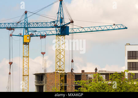 Stadtentwicklung Blick auf die Silhouetten von zwei hohen industriellen Turmdrehkrane am Bau neuer Ziegelgebäude mit Arbeitern in harte Hüte sie daran arbeiten und gegen BR Stockfoto