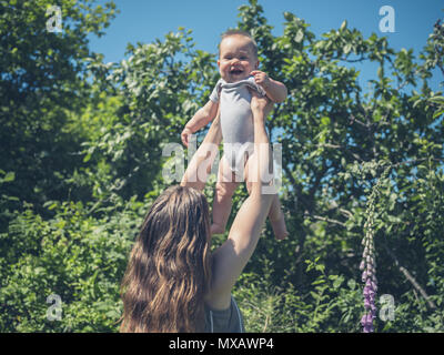 Eine junge Mutter hebt Ihr Baby in der Luft in der freien Natur Stockfoto
