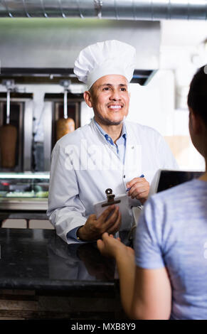 Fröhliche reifer Mann kochen, Auftrag vom Kunden am Counter in Fast-Food-Restaurant Stockfoto