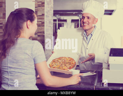 Reifer Mann Koch in Uniform Holding frisch gebackene Pizza in der Hand im Restaurant Stockfoto