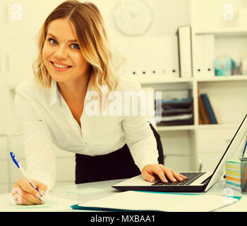 Aufmerksame Mädchen schreibt etwas auf ein Blatt Papier in modernen Büro Stockfoto