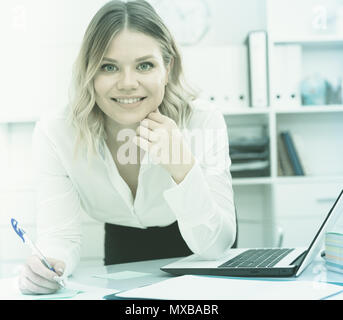 Aufmerksame Mädchen schreibt etwas auf ein Blatt Papier in modernen Büro Stockfoto