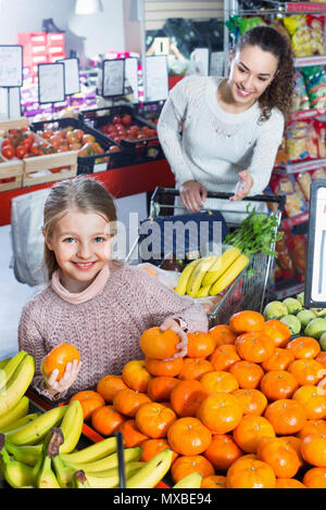 Fröhliche positive lächelnde Mutter und kleine hübsche Tochter kaufen süße Zitrusfrüchte Stockfoto