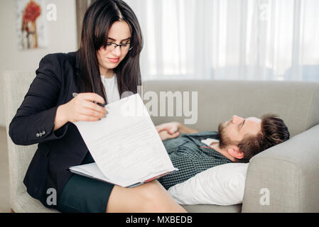 Betonte Mann liegt auf Sofa bei psychotherapeut Rezeption. Ärztin schreibt Notizen in Notepad, professionelle Psychologie Unterstützung Stockfoto
