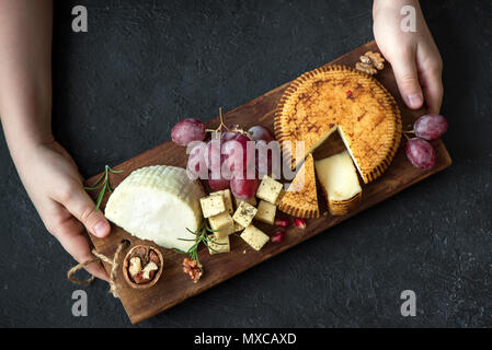 Käseplatte mit verschiedenen Käsesorten, Trauben, Nüsse und Hände der Käser auf schwarzem Hintergrund. Italienischen Käse und Obstteller. Stockfoto
