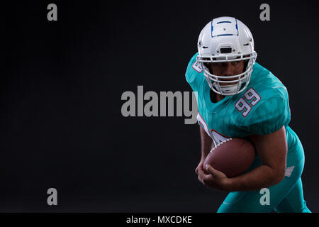Agressive American football Sportler Player auf schwarzem Hintergrund in Aktion ausgeführt wird. Sport Tapete mit Copyspace. Stockfoto