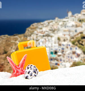 Tropischen Thema mit unscharfen Hintergrund mit Santorin, der griechischen Insel Architektur in den Hintergrund und eine orange Koffer und Star Shell in der Front Stockfoto