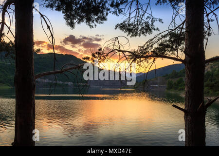 Zwei Pine Tree Silhouetten framing reflektierende, Golden Lake Zavoj in einer dramatischen Sonnenuntergang Stockfoto