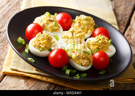 Russische Eier gefüllt mit Thunfisch und Avocado serviert mit Tomaten und Frühlingszwiebeln close-up auf einem Teller auf dem Tisch. Horizontale Stockfoto