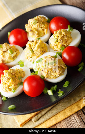 Russische Eier gefüllt mit Thunfisch und Avocado serviert mit Tomaten und Frühlingszwiebeln close-up auf einem Teller. Vertikale Stockfoto