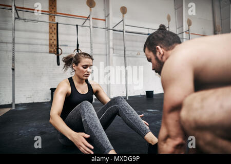 Passen junge Mann seine weiblichen Trainingspartner helfen Sie knirschen auf dem Boden einer Turnhalle während eines Training Session Stockfoto