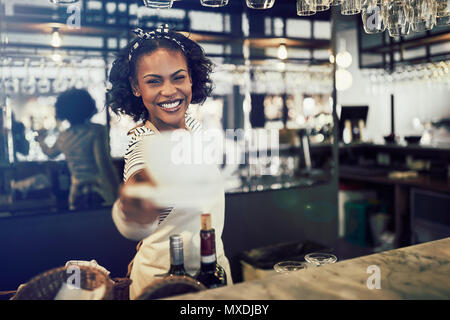 Junge afrikanische Barista lächelnd, während hinter der Theke eines angesagten Cafes und hielt eine frische Tasse Kaffee stehend Stockfoto