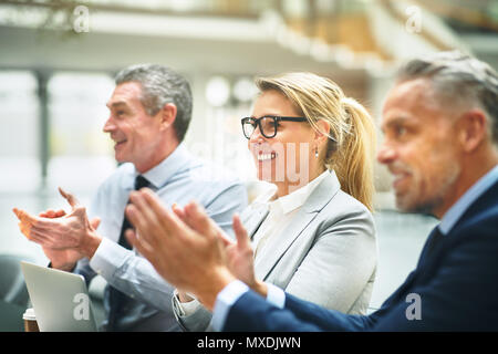 Reifen Gruppe von Geschäftsleuten sitzen zusammen an einem Tisch in einem modernen Büro lächelnd und Händeklatschen nach einer Präsentation Stockfoto