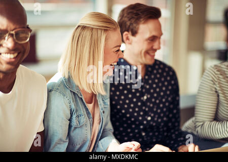 Lachende junge geschäftsfrau im Gespräch mit einer Gruppe von Kollegen sitzen zusammen in einem Büro Stockfoto