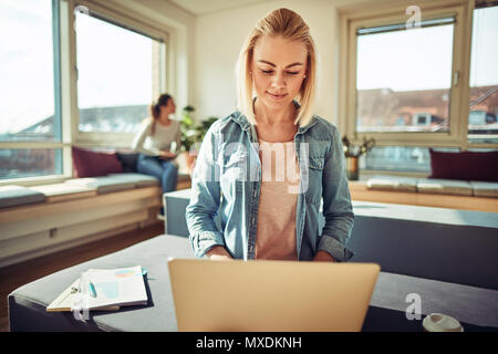Schwerpunkt junge Geschäftsfrau online arbeiten mit einem Laptop beim Sitzen auf ihrem Schreibtisch mit Kollegen sprechen im Hintergrund Stockfoto