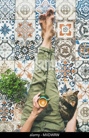 Weichen gemütlichen Foto eines Mädchens in warmen Pullover und rote Wolle Socken auf dem Bett mit einer Tasse Tee/Kaffee in Händen, Top View Point. Morgen, Winter und Personen Konzept der jungen Frau mit Orange Cat. Stockfoto