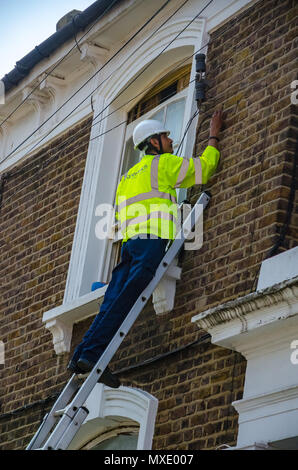 Eine Openreach Ingenieur auf eine Leiter arbeiten an einer Telefonleitung eine Verbindung zu einem Wohnimmobilien. Stockfoto