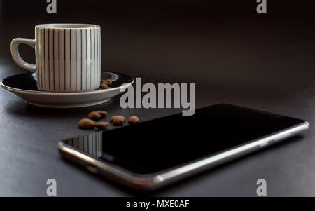 Smartphone neben Kaffee auf dunklem Leder Oberfläche mit Kaffeebohnen Stockfoto