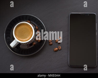 Smartphone neben Kaffee auf dunklem Leder Oberfläche mit Kaffeebohnen Stockfoto