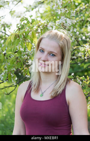 Portrait von Cool lächelnde junge blonde Frau mit den blühenden Apfelbaum im Hintergrund. Vertikal. Stockfoto