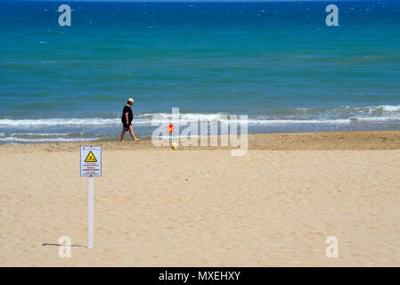 Person zu Fuß am Strand mit Warnzeichen für Meeresströmungen. Kein Schwimmen rote Fahne. Strand am Mittelmeer. Walker. Die Med, Spanien. Blaues Wasser. Gefahr Stockfoto