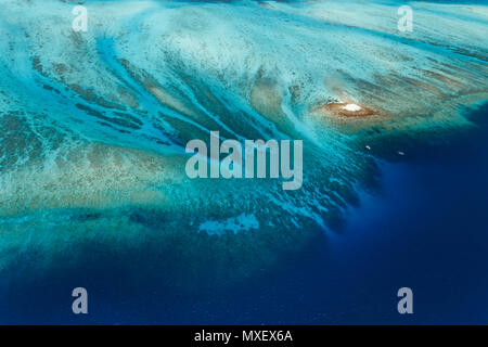 Aus der Vogelperspektive zwei Boote, die über einem großen Korallenriff schwimmen, das seichtes Atoll vom tiefen blauen Ozean trennt Stockfoto