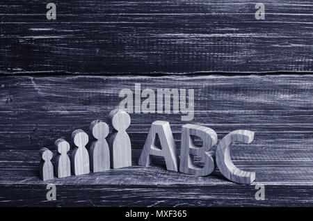 Hölzerne Figuren der Kinder stehen in einer Reihe von klein bis groß in der Nähe der Buchstaben des englischen Alphabets abc. Der Begriff der Bildung und Studium, eine scho Stockfoto