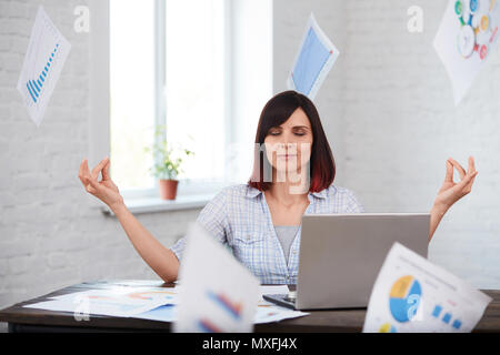 Müde Arbeiterin meditiert im Büro mit fallender Papiere um. betonte Frau, die versucht, nach unten und denken nicht an Frist zu beruhigen. Überarbeitung, deadli Stockfoto