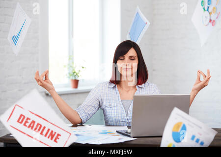 Müde Arbeiterin meditiert im Büro mit fallender Papiere um. betonte Frau, die versucht, nach unten und denken nicht an Frist zu beruhigen. Überarbeitung, deadli Stockfoto