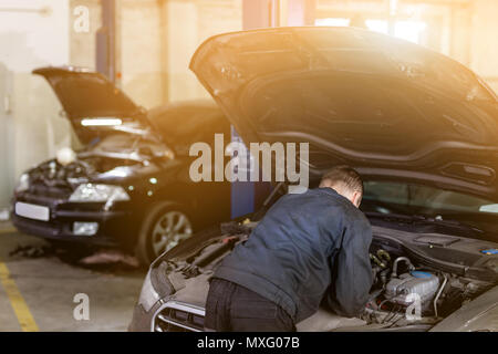 Mehanic tun Check-up unter die Haube geöffnet Auto. Werkzeuge über schmutzige Motor Zimmer. Auto Service und Wartung. Getönt. Stockfoto