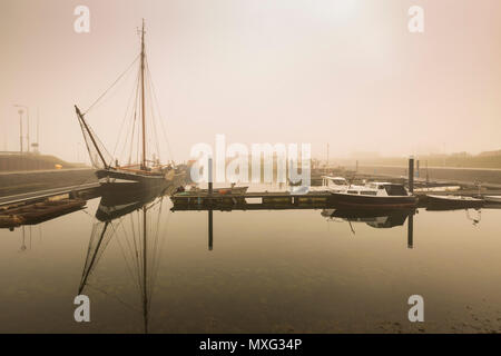 Angelboote/Fischerboote warten verzögert Abfahrt im Hafen von Bruinisse, Zeeland, durch dichten Nebel bei Sonnenaufgang. Ruhiges Wasser und einer ruhigen Landschaft Witz Stockfoto