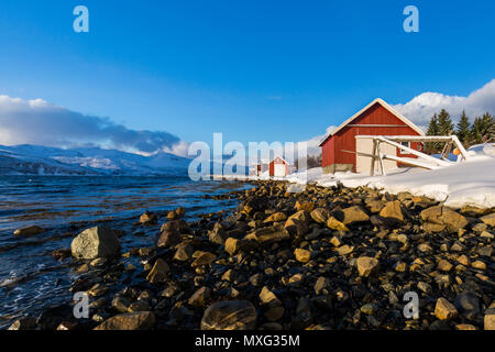 Typische norwegische warme und gemütliche Haus befindet sich am See an einem Fjord in Troms Grafschaft, Norwegen. Die Sonne über dem Horizont niedrig eingestellt ist und der Himmel ist Stockfoto