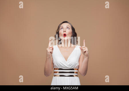 Fragte sich Frau Finger zeigen auf Kopieren. Emotion und Gefühl Konzept. Studio shot, Indoor, auf hellbraunem Hintergrund isoliert Stockfoto