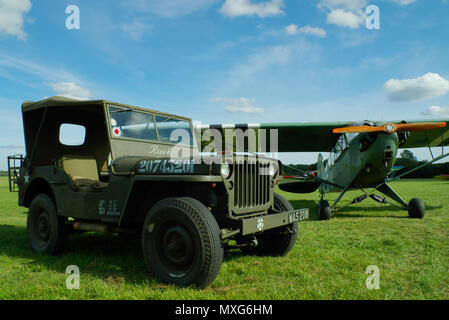 Oldtimer-Flugzeug und Auto. Piper Cub-Flugzeug mit US Willys Jeep. Willys MB Kriegsfahrzeug. Grasfeld. Invasionsstreifen Stockfoto