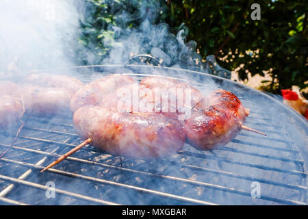 Würstchen chorizos Grillen im Freien an einem sonnigen Tag, viel Rauch, salsiccia fast bereit, gut zubereitet Stockfoto