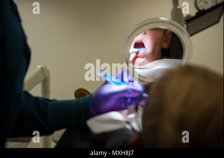 Channing Wray, hält einen Spiegel zu sehen, wie sein Zahnarzt seine Zähne während der "Kleinen Zähne, Big Smile" Fall an der Air Base Ramstein, Deutschland, Nov. 5, 2016 reinigt. Die Veranstaltung war eine Art und Weise für Kinder bis 10 Jahre ihre Zähne überprüfen oder in einer Umgebung auf ihre Altersgruppe zugeschnitten gereinigt zu bekommen. Laut dem Zentrum für Krankheit und Steuerung, Karies ist eine der häufigsten chronischen Erkrankungen der Kindheit in den Vereinigten Staaten. Unbehandelte Hohlräume können Schmerzen und Infektionen, die auf Probleme mit dem Essen, sprechen, spielen und lernen. (U.S. Air Force Foto von Flieger 1. Klasse Stockfoto