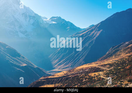 Schöne Sicht auf die Berge Tal. Landschaft mit Hügeln, Trails und schneebedeckten Berg gegen den blauen Himmel bei Sonnenaufgang in Nepal. Schneebedeckten Gipfeln des Himalay Stockfoto