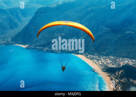 Gleitschirmfliegen in den Himmel. Gleitschirm Tandem über das Meer mit blauem Wasser, Strand und Berge im Sunrise fliegen. Luftaufnahme von Gleitschirm und blauen Lago Stockfoto